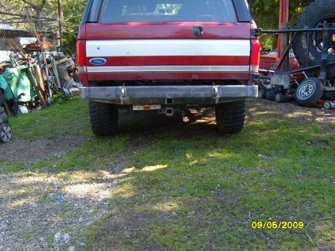 1989 Ford Bronco - Rear view of a red 1989 Ford Bronco, a chrome stripe on the tailgate and an aftermarket rear bumper with a tow hitch.