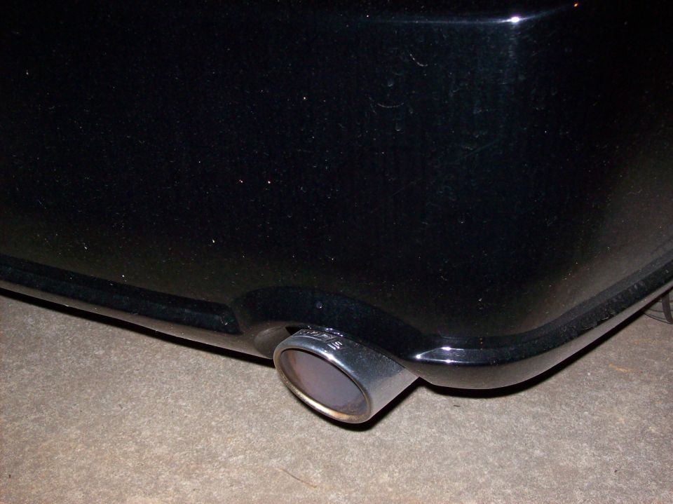 Black car's chrome exhaust pipe visible from the rear quarter panel, with a watermark reading SUPERMOTORS.NET