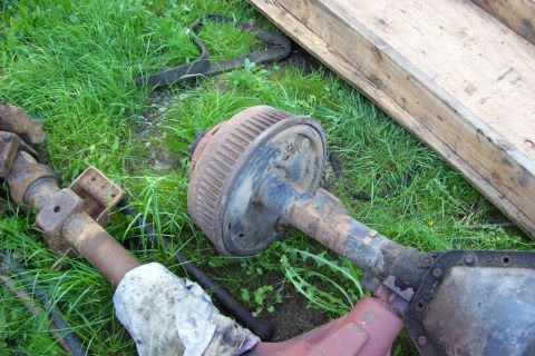 1995 Ford Bronco - Front axle assembly with drum brake, likely from an older truck or SUV, lying on grass.