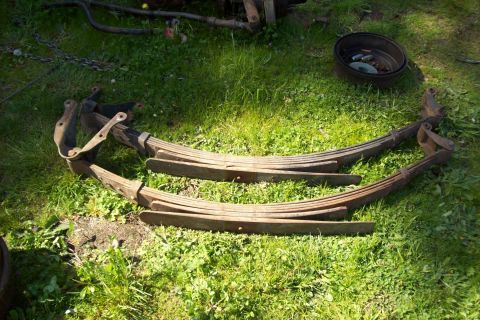 1995 Ford Bronco - Two sets of rusty leaf springs are laid out on a grassy area, possibly for a vehicle restoration project.