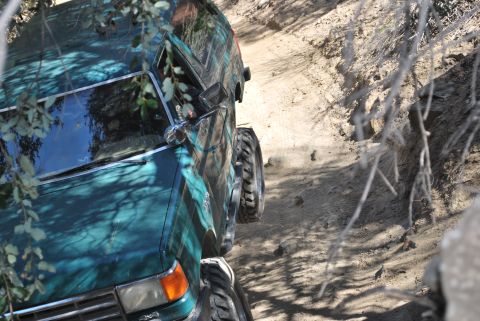 1996 Ford Bronco - A vehicle navigates a tight off-road trail, its tires gripping the loose dirt.