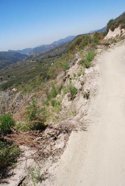1996 Ford Bronco - A dirt road winds along a steep mountainside with a valley and distant mountains in the background.