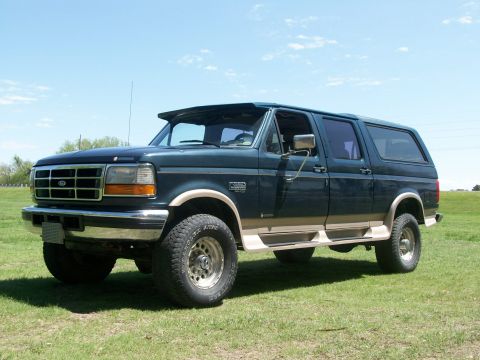1995 Ford C-350 (Centurion Conversions) - This modified SUV features a two-tone paint scheme and aftermarket wheels, sitting on a grassy field under a clear blue sky.