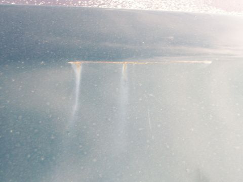 1995 Ford C-350 (Centurion Conversions) - Close-up of a dark green painted body panel showing a horizontal seam line with rust bleeding through and two rust-colored streaks running…