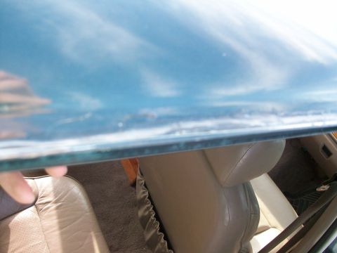 1995 Ford C-350 (Centurion Conversions) - Edge of a glass pane held up over a tan leather seat and carpeted vehicle interior in sunlight.