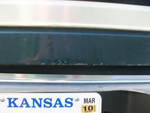 1995 Ford C-350 (Centurion Conversions) - Close-up of a dark green rear bumper and a Kansas license plate, showing some wear and tear on the paint.
