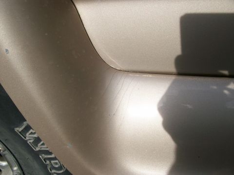 1995 Ford C-350 (Centurion Conversions) - Close-up of a tan vehicle's side panel showing scratches and a portion of a tire.