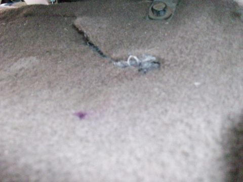 1995 Ford C-350 (Centurion Conversions) - Close-up of damaged interior floor carpet that is torn and scorched, with a bolt visible at the top edge.