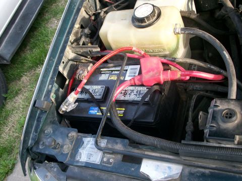 1995 Ford C-350 (Centurion Conversions) - Close-up view of the engine bay, focusing on the battery and associated wiring, with a coolant reservoir visible.