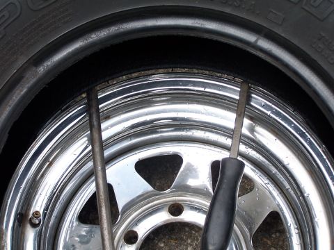 1990 Ford Bronco - Tools are used to remove a tire from a chrome wheel. The tire tread is visible at the top.