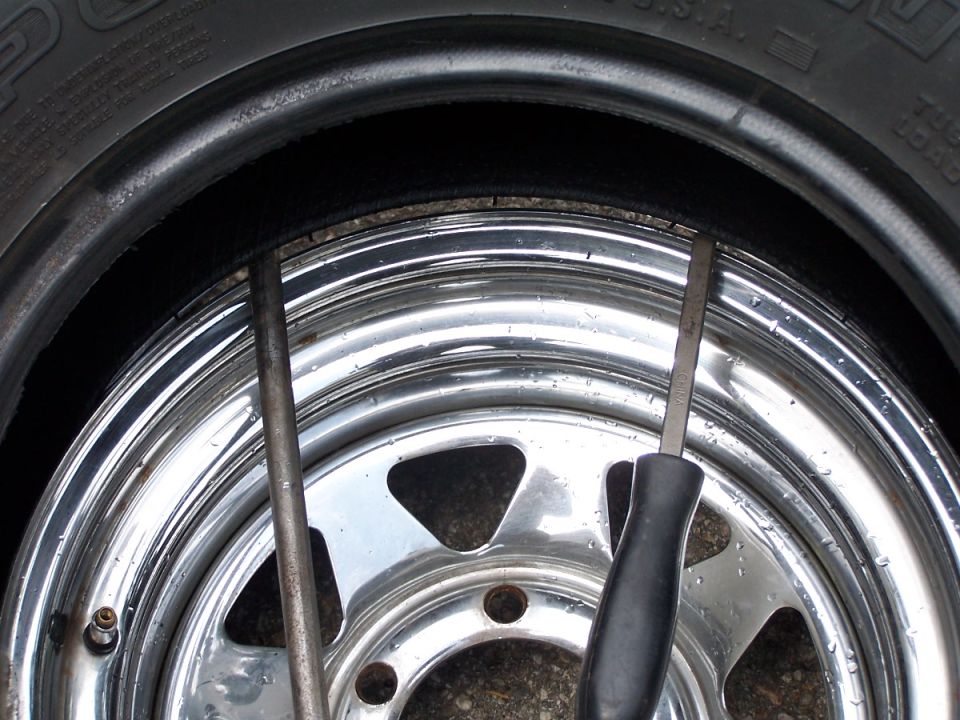 Close-up of a tire and chrome rim with two screwdrivers being used to pry the tire off the rim