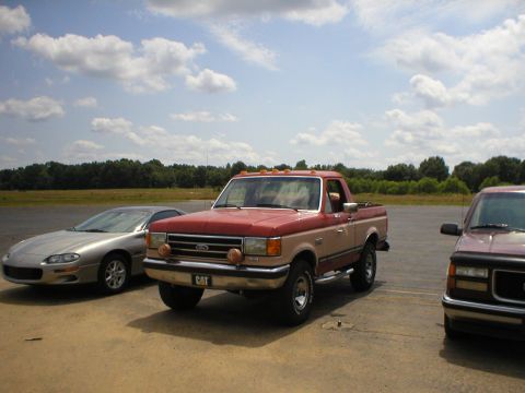 1983 Ford Bronco - Ford F-Series pickup truck and Chevrolet Camaro parked outdoors under a cloudy sky.