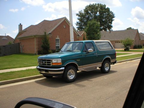 1983 Ford Bronco - A green Ford Bronco with tan trim is parked on the side of a residential street.