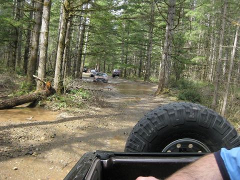 1992 Ford Bronco - A group of vehicles navigates a wet, wooded trail, kicking up mud as they go.