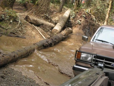 1992 Ford Bronco - A brown Ford Bronco navigates a muddy obstacle course with fallen logs.