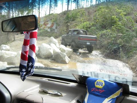 1992 Ford Bronco - A dark pickup truck navigates a rocky, muddy trail, viewed from the interior of another vehicle.