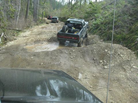 1992 Ford Bronco - Several vehicles navigate a challenging, muddy trail through a wooded area.