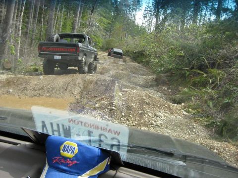 1992 Ford Bronco - Two off-road vehicles navigate a muddy, wooded trail.