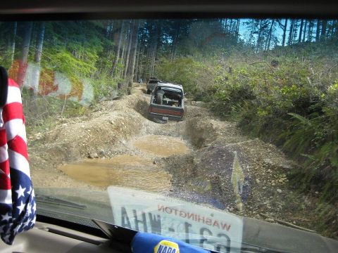 1992 Ford Bronco - Vehicles traverse a difficult off-road path with deep mud and water obstacles.