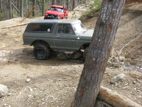1992 Ford Bronco - A green SUV navigates a rocky, off-road trail with a red truck behind it.