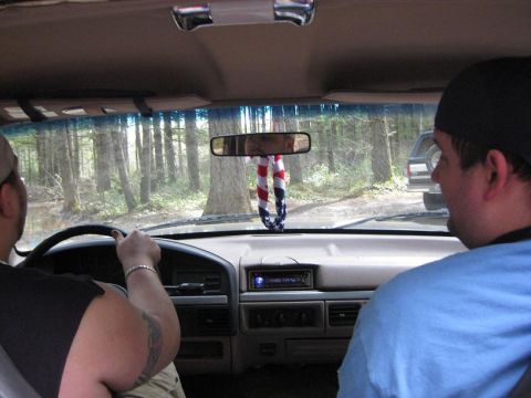 1992 Ford Bronco - View from inside a vehicle as it drives down a dirt road surrounded by a dense forest.