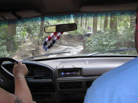 1992 Ford Bronco - The interior of a 1992 Ford Bronco is seen from the passenger seat as it navigates a muddy trail with another vehicle in the distance.