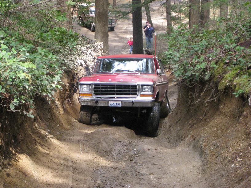 Red Ford truck with a black grille driving on a dirt path