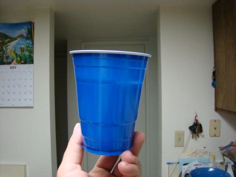 1989 Ford Bronco - A blue plastic cup is held in a hand, with a calendar visible on the wall.