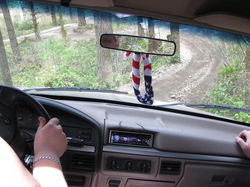 Interior view of a vehicle driving on a dirt road with an American flag air freshener