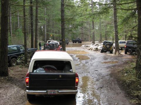 1992 Ford Bronco - Off-road vehicles navigate a muddy path through a dense forest during an event.