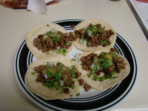 1989 Ford Bronco - A plate of four tacos topped with meat, onions, cilantro, and salsa sits on a counter.
