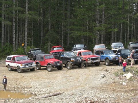1992 Ford Bronco - A group of off-road vehicles, including a 1992 Ford Bronco, are gathered in a wooded area.
