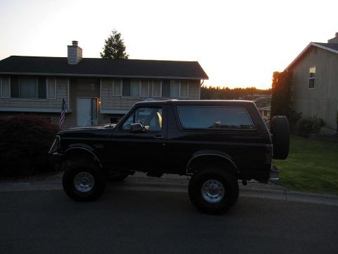1992 Ford Bronco - Side view of a lifted black 1992 Ford Bronco with a spare tire mounted on the back.