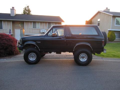 1992 Ford Bronco - A lifted black Ford Bronco is parked on a residential street with a house in the background.