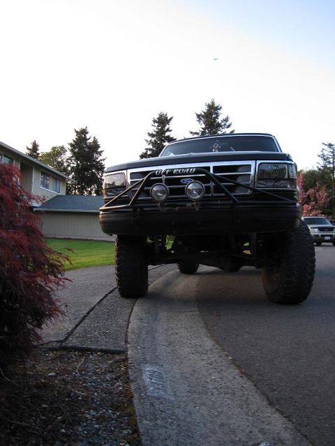 1992 Ford Bronco - A lifted 1992 Ford Bronco with an aftermarket bumper and off-road lights is parked on a residential street.