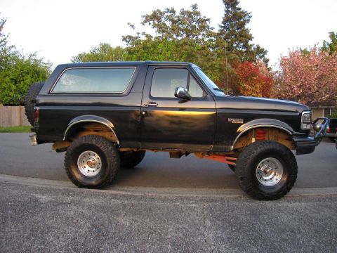1992 Ford Bronco - This lifted black Ford Bronco is parked on a residential street during the day.