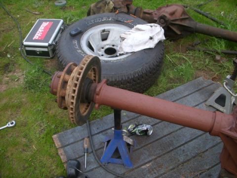 1995 Ford Bronco - Front axle assembly for a Ford Bronco, resting on a jack stand with a tire nearby.