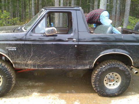 1992 Ford Bronco - A muddy 1992 Ford Bronco is seen from the side, with a person partially visible in the rear cargo area.