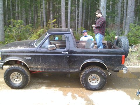 1992 Ford Bronco - A black 1992 Ford Bronco is seen from the side, with several people riding in the open rear.