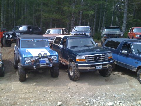 1992 Ford Bronco - A blue 1992 Ford Bronco, modified for off-roading, is parked in a lot with several other trucks and SUVs.