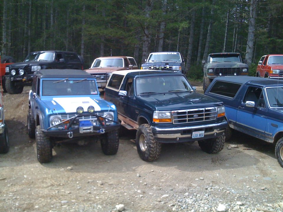 Blue 1992 Ford Bronco with off-road lights and winch, parked next to a dark green Bronco