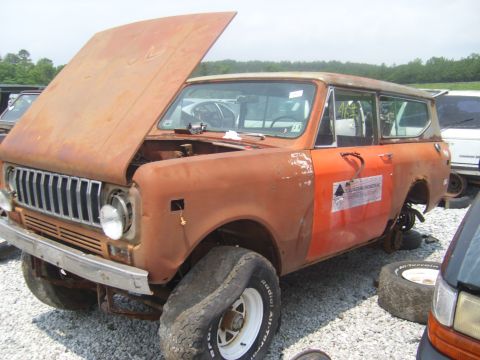 1994 Ford Bronco - This weathered SUV sits in a junkyard with its hood ajar and a flat tire, showing signs of significant wear.