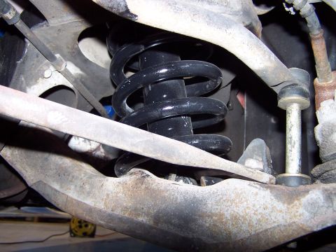 1973 Ford Ranchero - Close-up of a front suspension corner shot from below, showing a black-painted coil spring seated between the upper and lower control arms.…