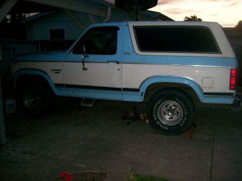 1982 Ford Bronco - This two-tone blue and white SUV is viewed from the side, showing its tinted windows and a step bar below the doors.