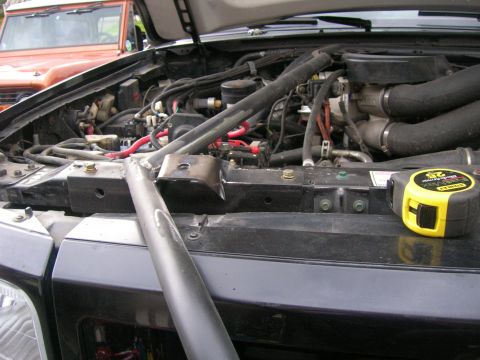 1996 Ford Bronco - Close-up of an engine bay, with a tape measure on the grille. Another vehicle is parked behind it.