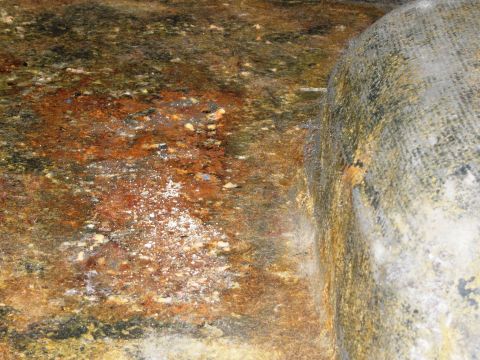 1986 Ford Bronco - A close-up view of a heavily corroded metal surface with white mineral deposits, adjacent to a textured concrete element.