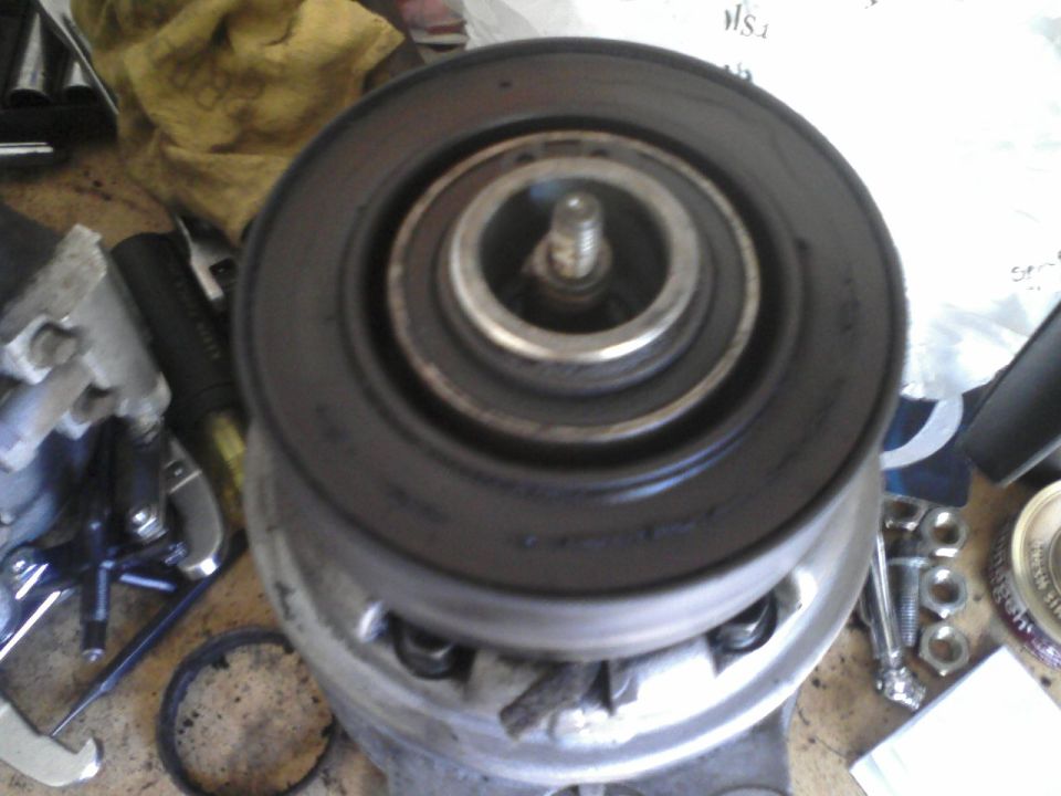 Pulley assembly with a black outer ring and a central bolt, resting on a surface with tools and nuts