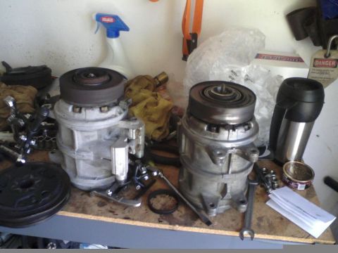 1986 Ford Bronco - Two automotive air conditioning compressors are displayed on a shelf, alongside various tools and cleaning supplies.