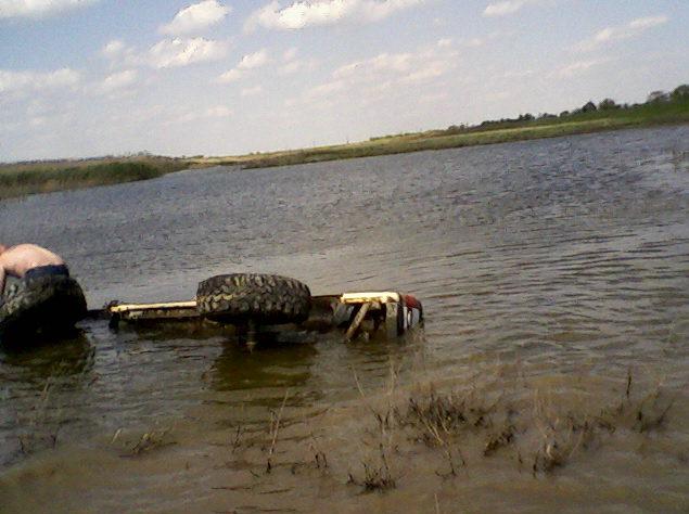 Vehicle partially submerged in water with a spare tire on top. Person visible on the left