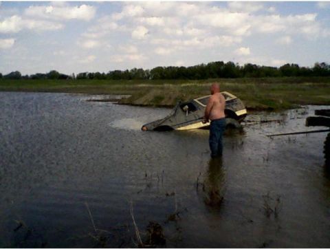 1990 Ford Bronco - A man stands beside a vehicle that is stuck in the water.